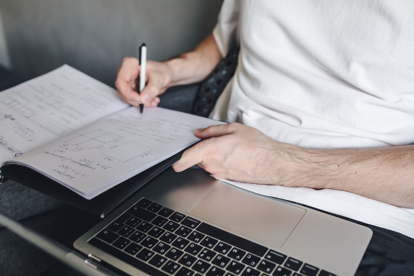 A person drafts notes beside an open laptop.