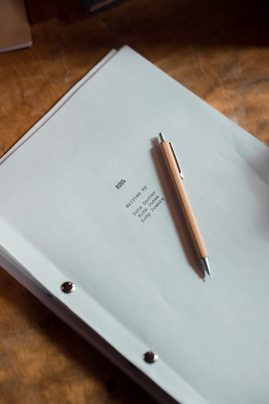A pen rests on printed script pages on a wooden desk.