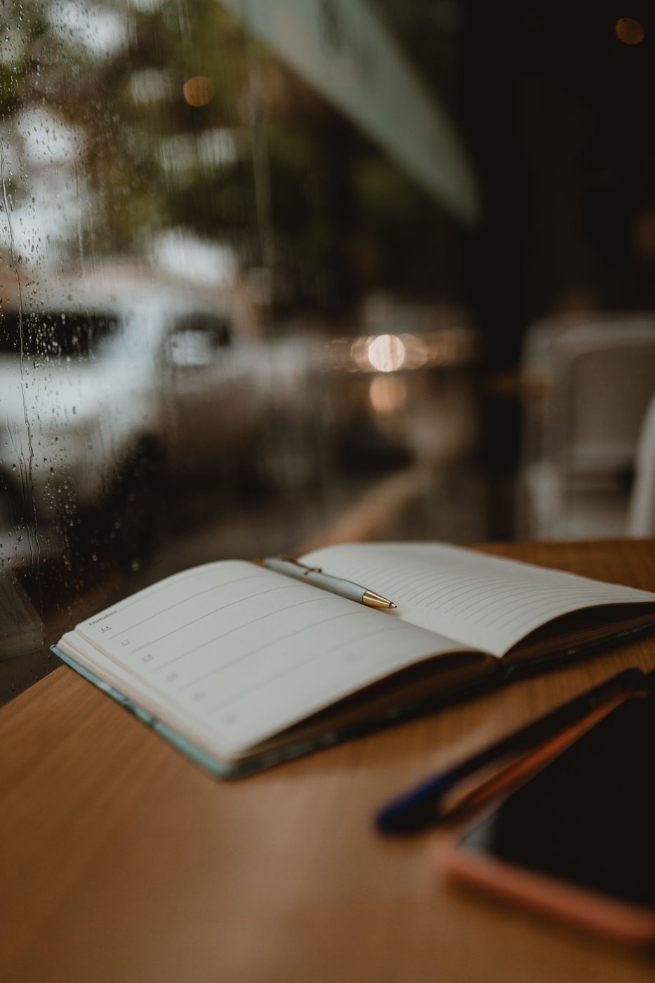 An open notebook and pen beside a rain-covered window.