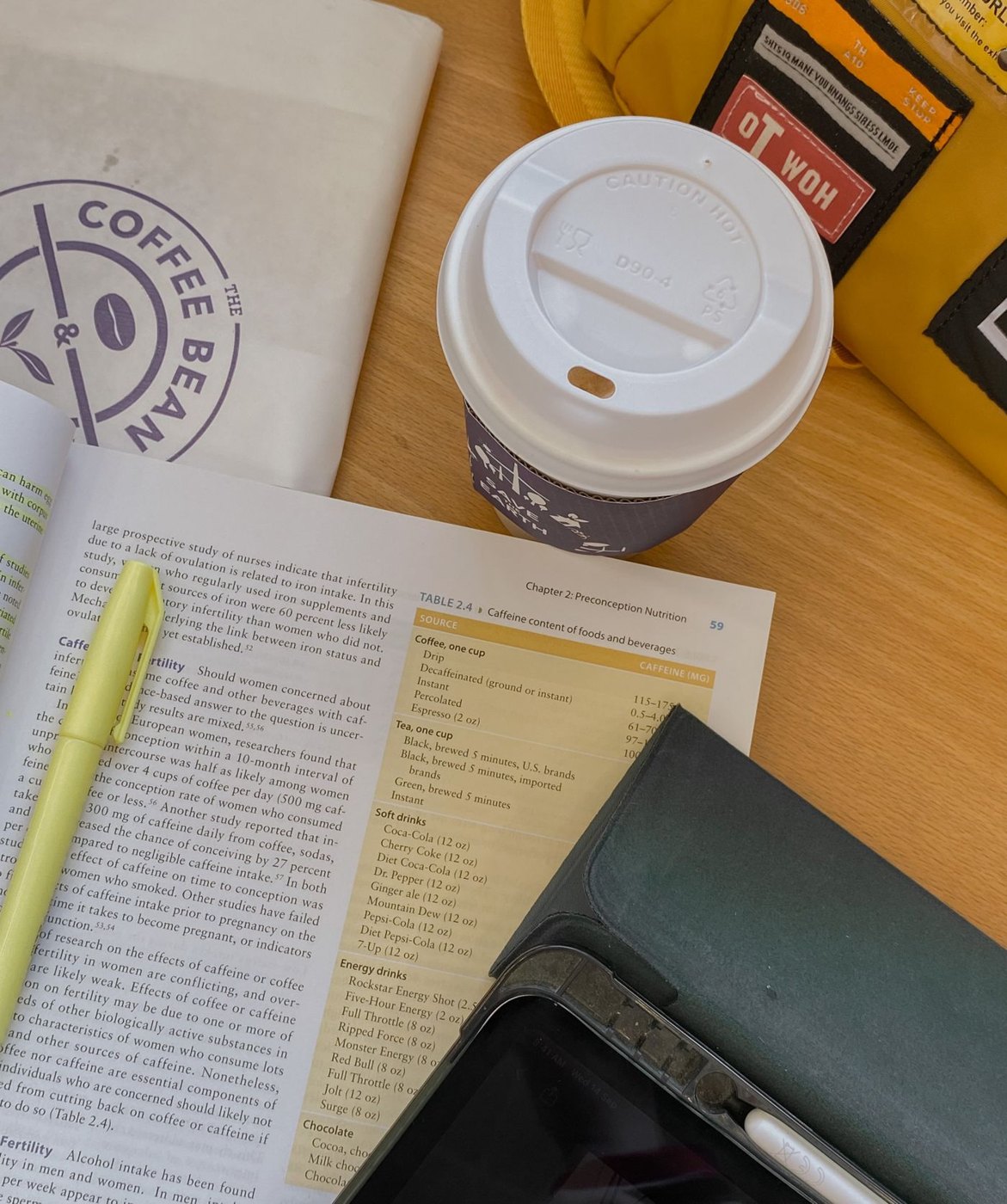 An open reference book with a highlighter beside a tablet and coffee.