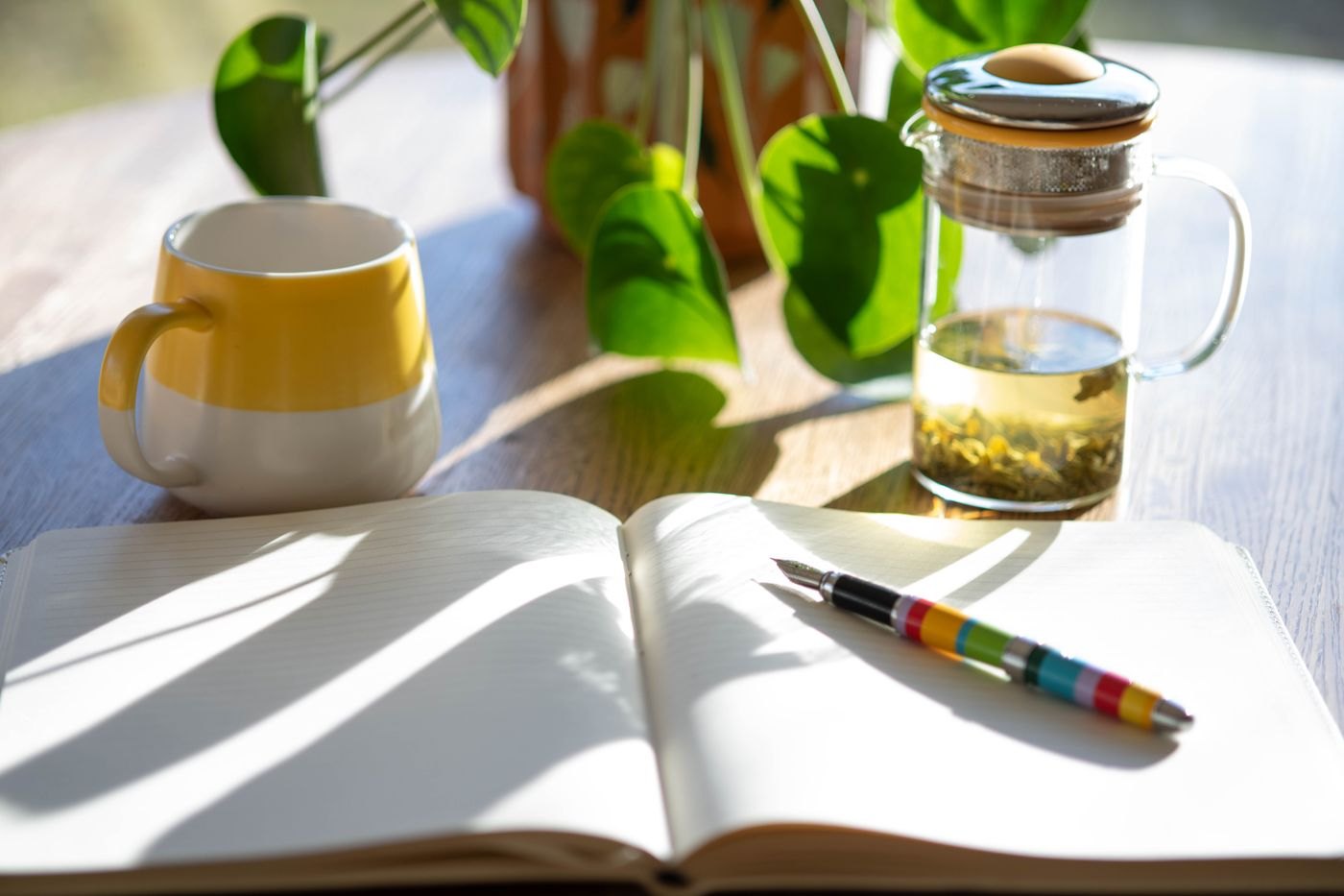 A sunlit writing desk with an open notebook, pen and mug.