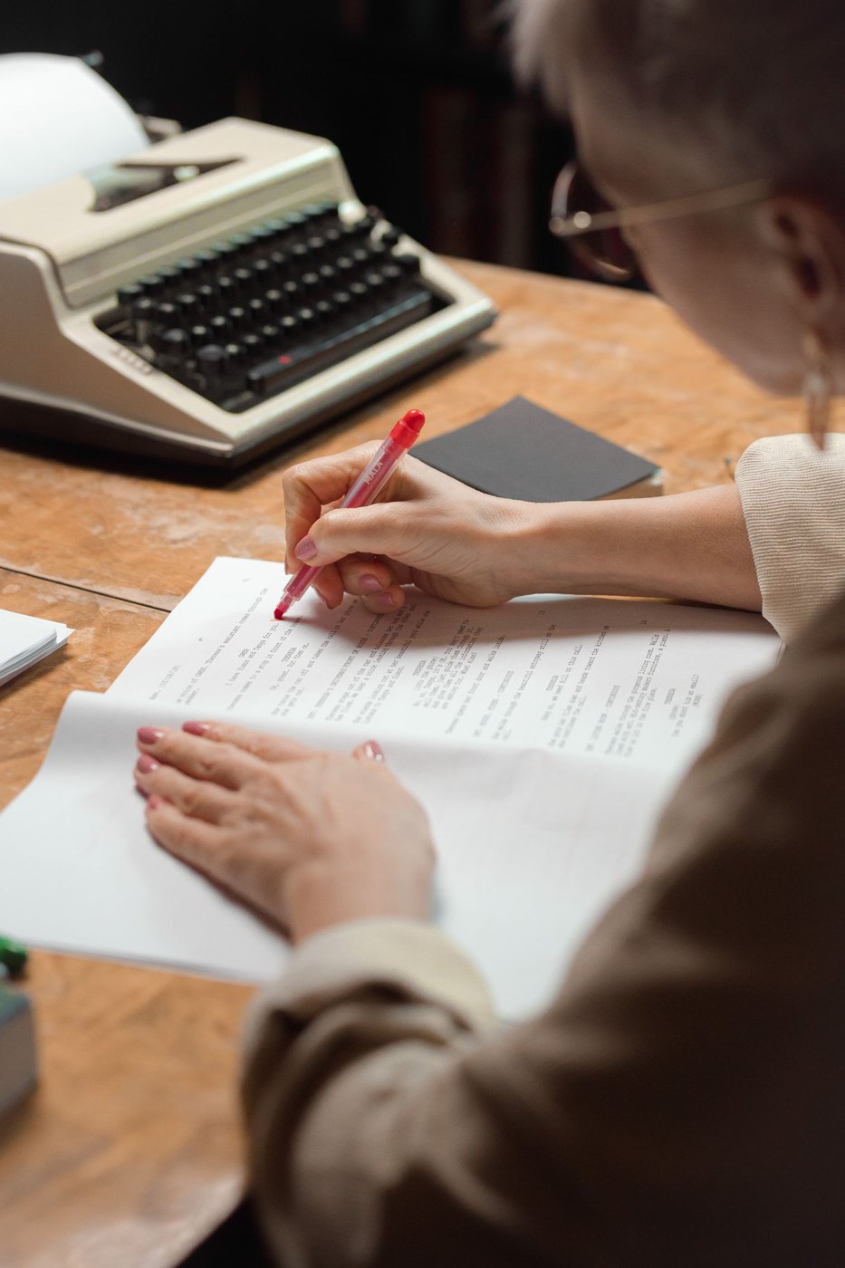A reader reviews manuscript pages beside a typewriter.