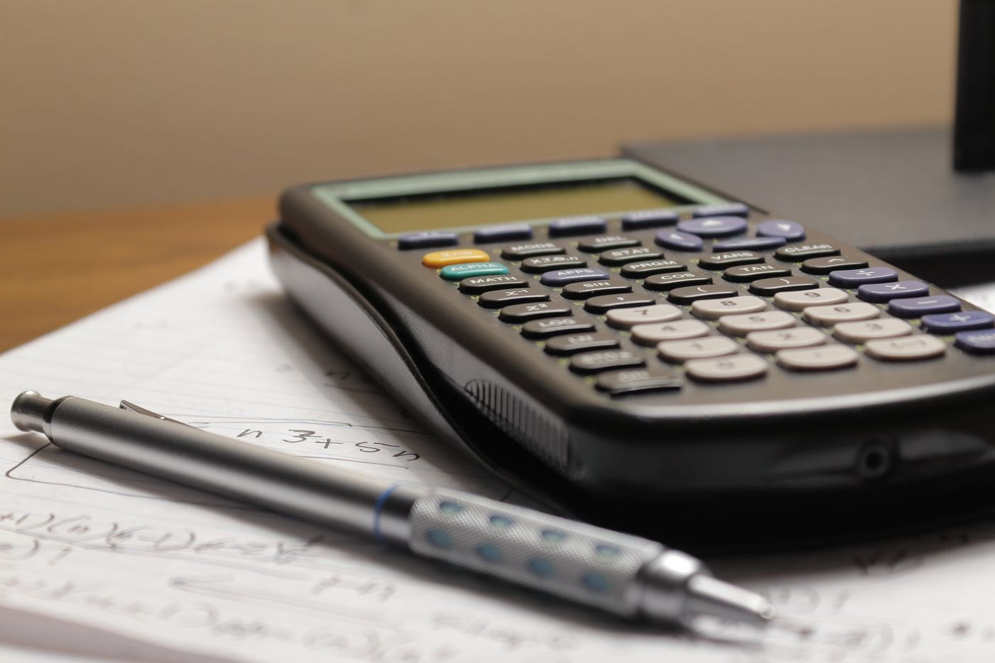 A calculator and pen rest on handwritten calculations.