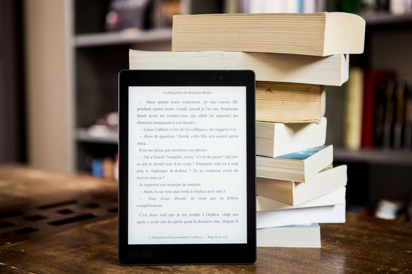 An e-reader displaying text beside a stack of printed books.
