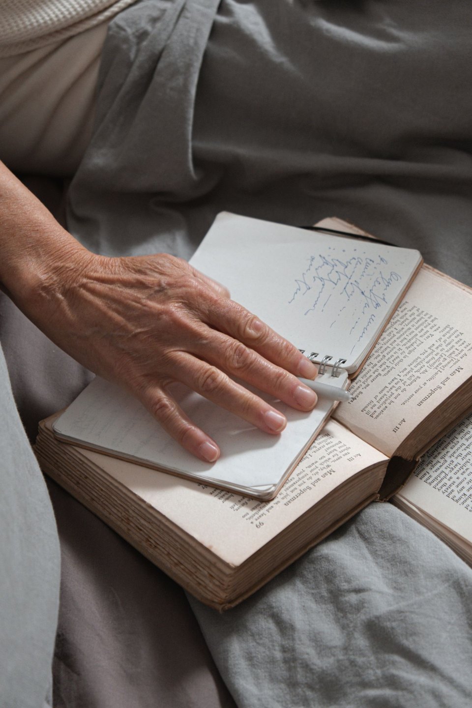 A hand holding a notebook over an open book.