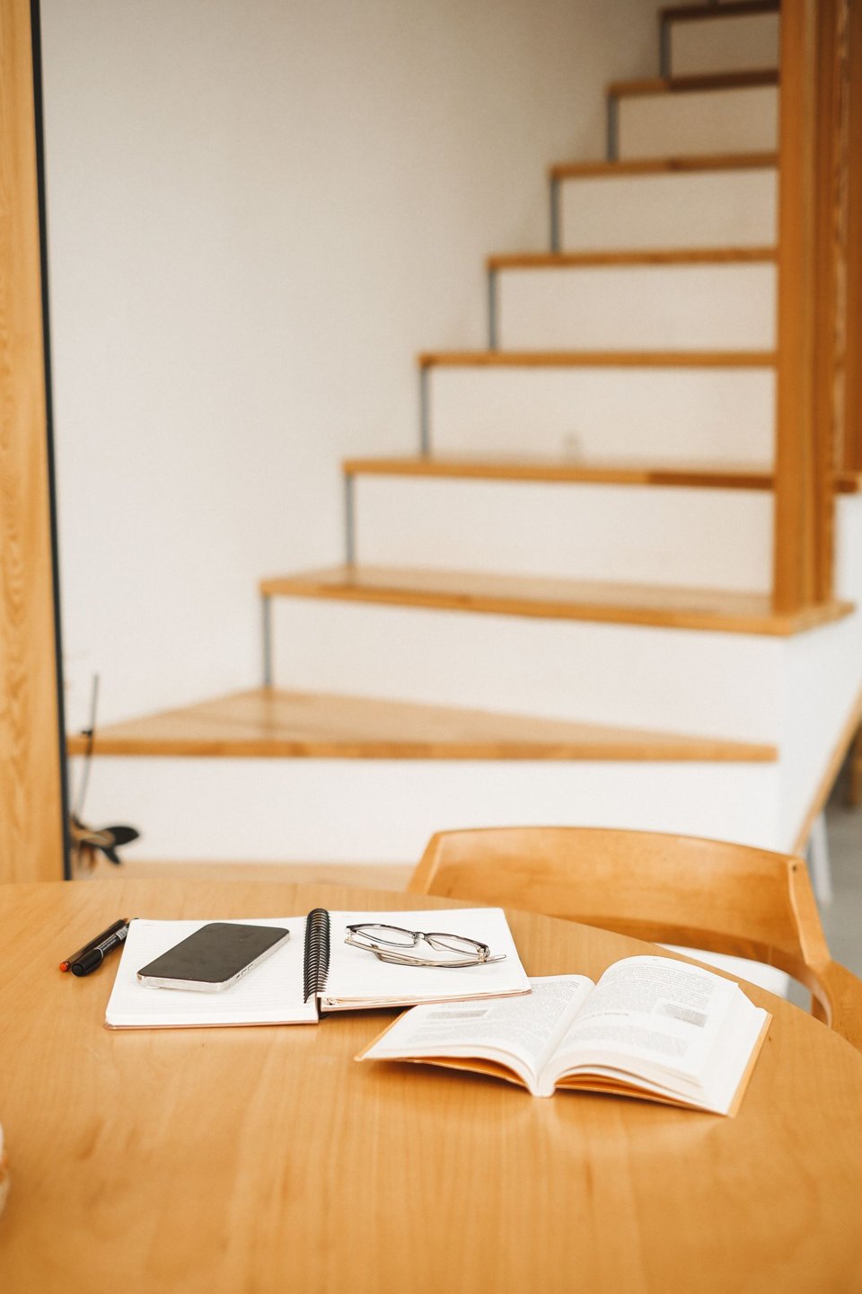 An open book, notebook and phone on a wooden table.