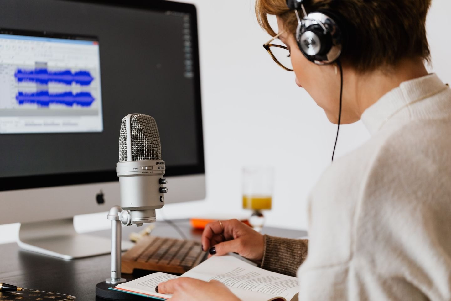 A person at a microphone with a book and audio recording screen.