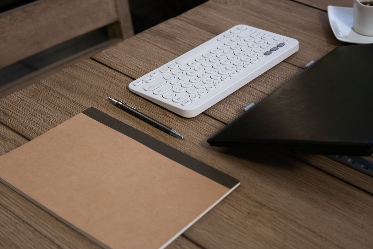 A plain notebook, pen and keyboard on a wooden desk.