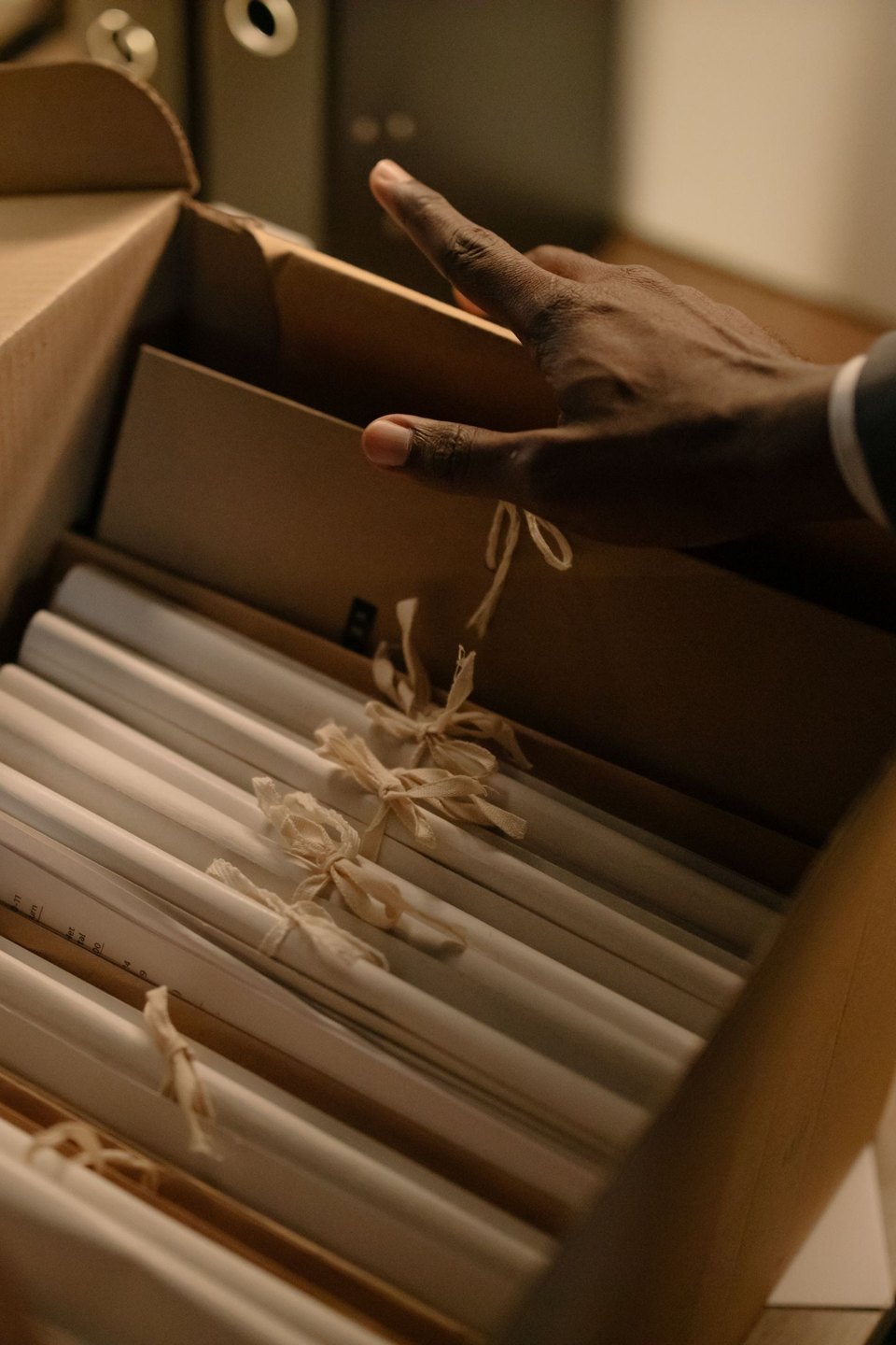A hand reaching into an archive box of paper files.